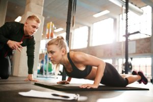 Indoor shot of young female exercising with personal trainer at gym. Fitness woman doing push ups with her personal trainer at health club.